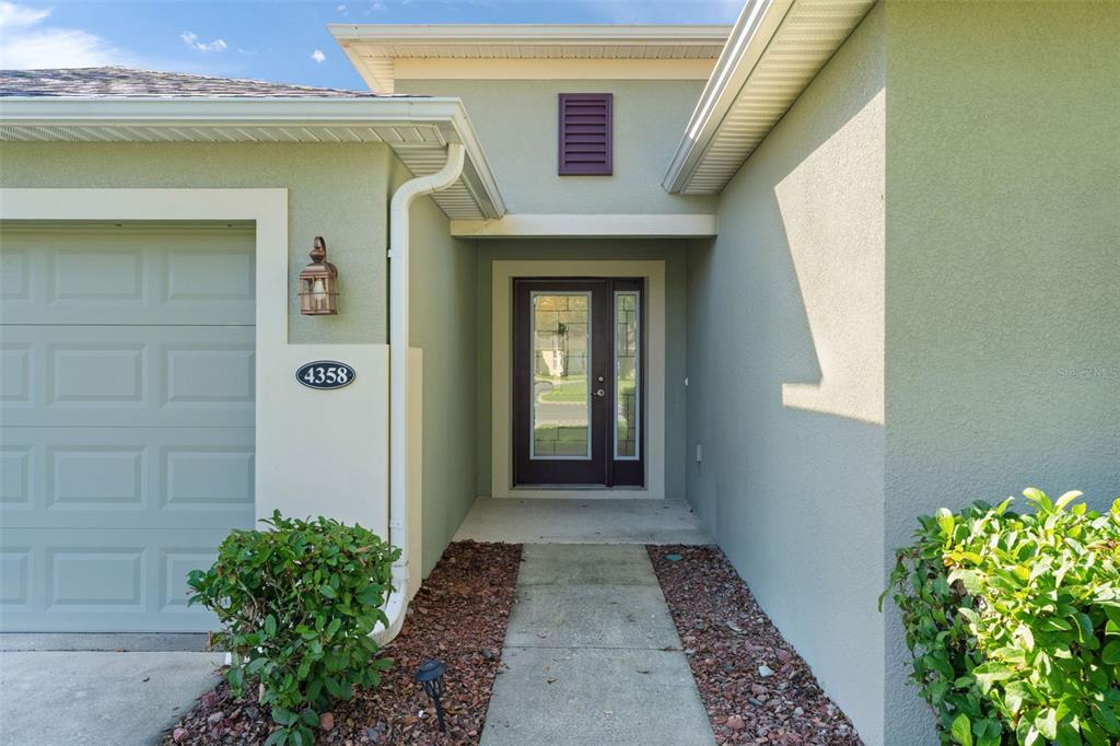 A single-story house with a two-car garage, light green stucco exterior, and a front lawn — 4358 ANTIETAM CREEK TRAIL, LEESBURG, FL