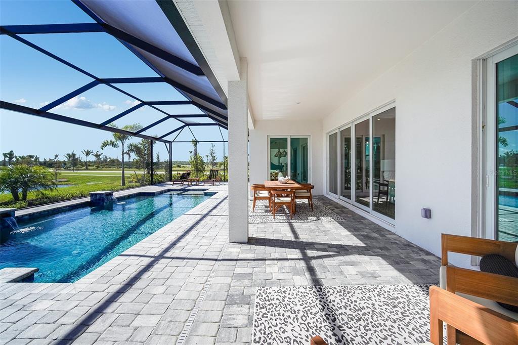 A covered patio features a swimming pool, dining set, and sliding glass doors to the home — 18939 CHERRYSTONE WAY, LAKEWOOD RANCH, FL