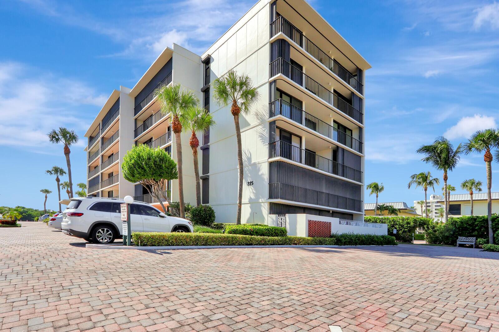 A multi-story apartment building with balconies and palm trees stands above a paved parking lot — 225 Beach Road # 204, Tequesta FL 33469, TEQUESTA, FL