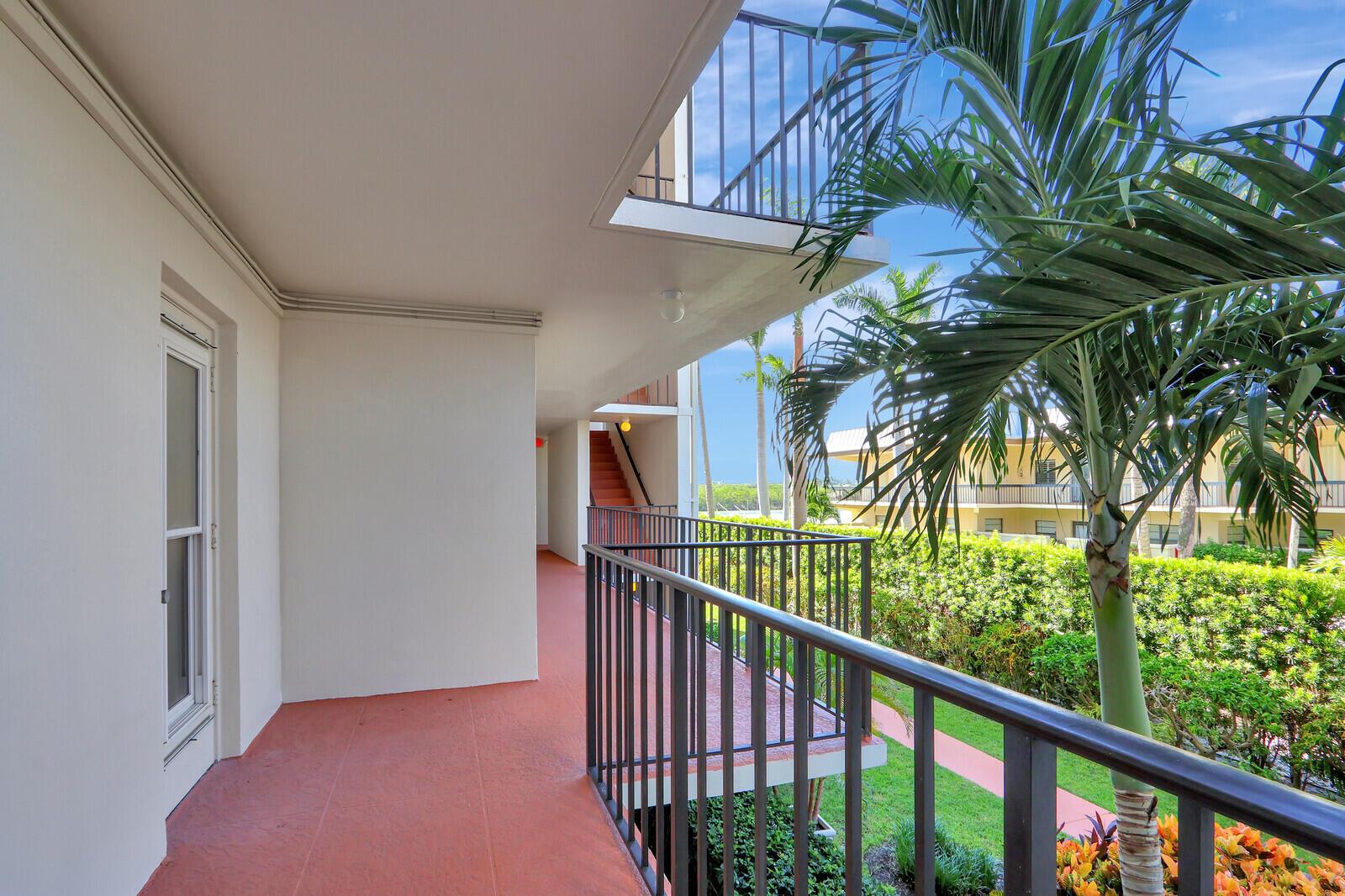 A covered outdoor walkway with a red floor, metal railings, and a palm tree — 225 Beach Road # 204, Tequesta FL 33469, TEQUESTA, FL
