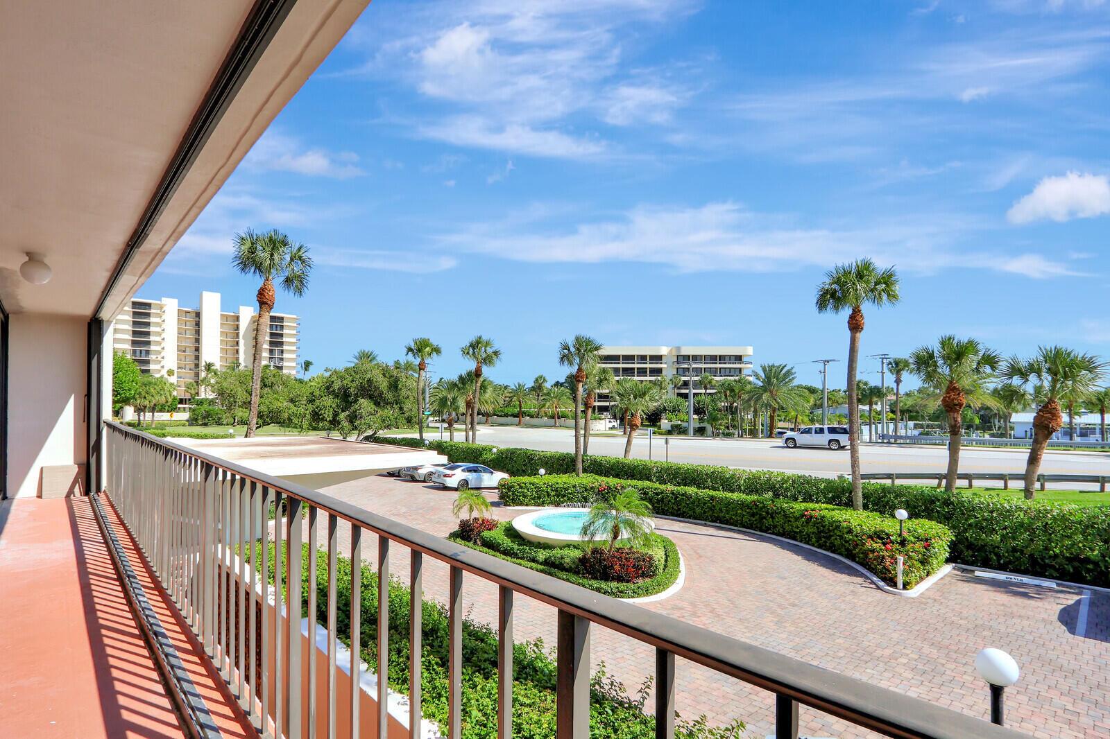 A balcony view overlooking a paved driveway, a small fountain, palm trees, and nearby buildings — 225 Beach Road # 204, Tequesta FL 33469, TEQUESTA, FL