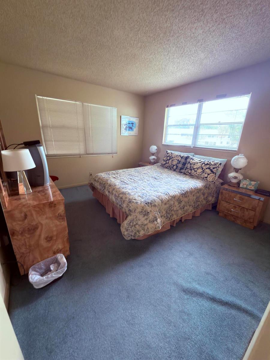 A bedroom with blue carpeting, a floral bedspread, and matching wood-grain furniture — 193 Prescott J # J, Deerfield Beach FL 33442, DEERFIELD BEACH, FL