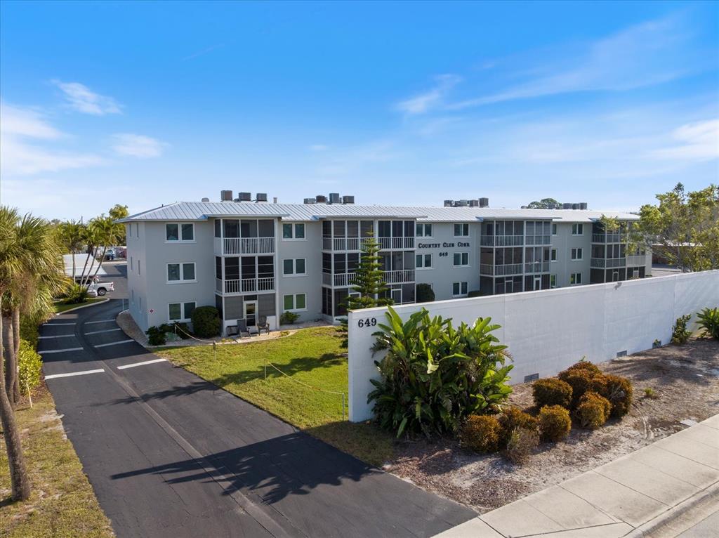 An exterior view of a three-story apartment building with screened balconies and a paved driveway — 649 TAMIAMI TRAIL S UNIT 305, VENICE, FL
