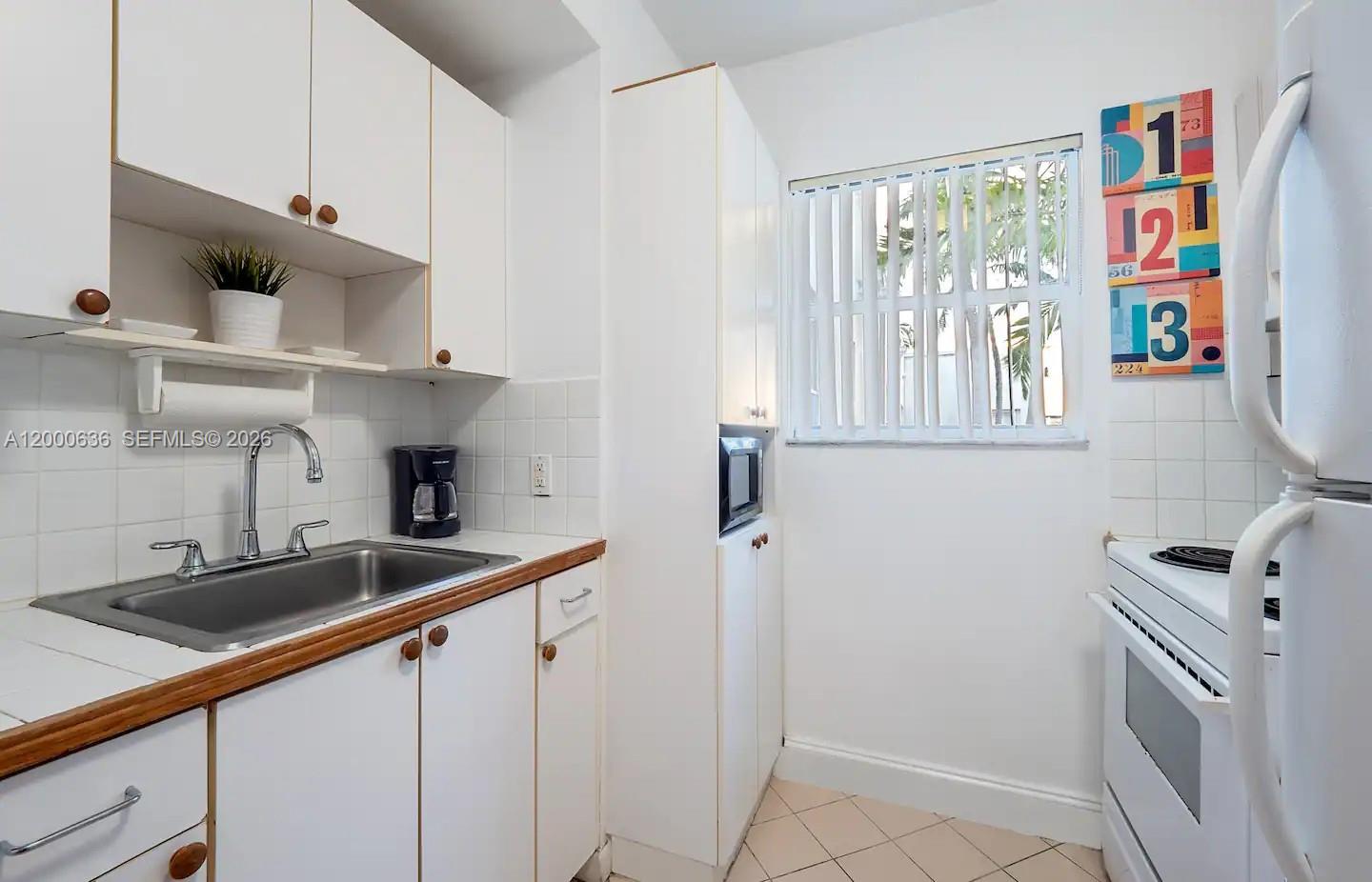 A small kitchen features white cabinets, a stainless steel sink, and a white stove — 2615 Collins Ave # 37, Miami Beach FL 33140, MIAMI BEACH, FL