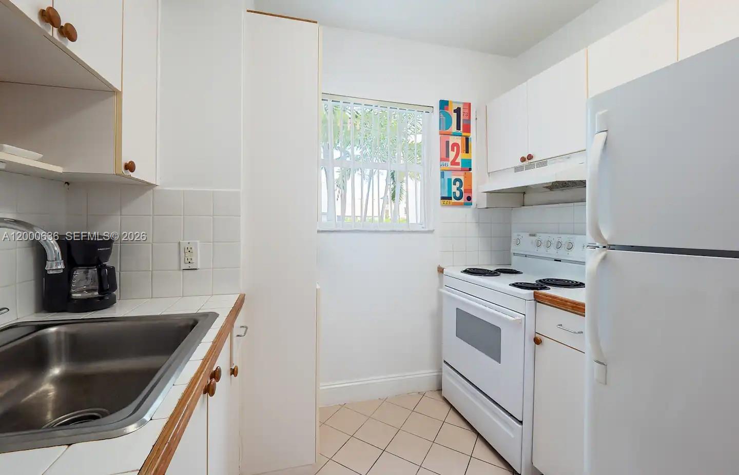 A small kitchen features white cabinets, white appliances, a tiled backsplash, and a window — 2615 Collins Ave # 37, Miami Beach FL 33140, MIAMI BEACH, FL
