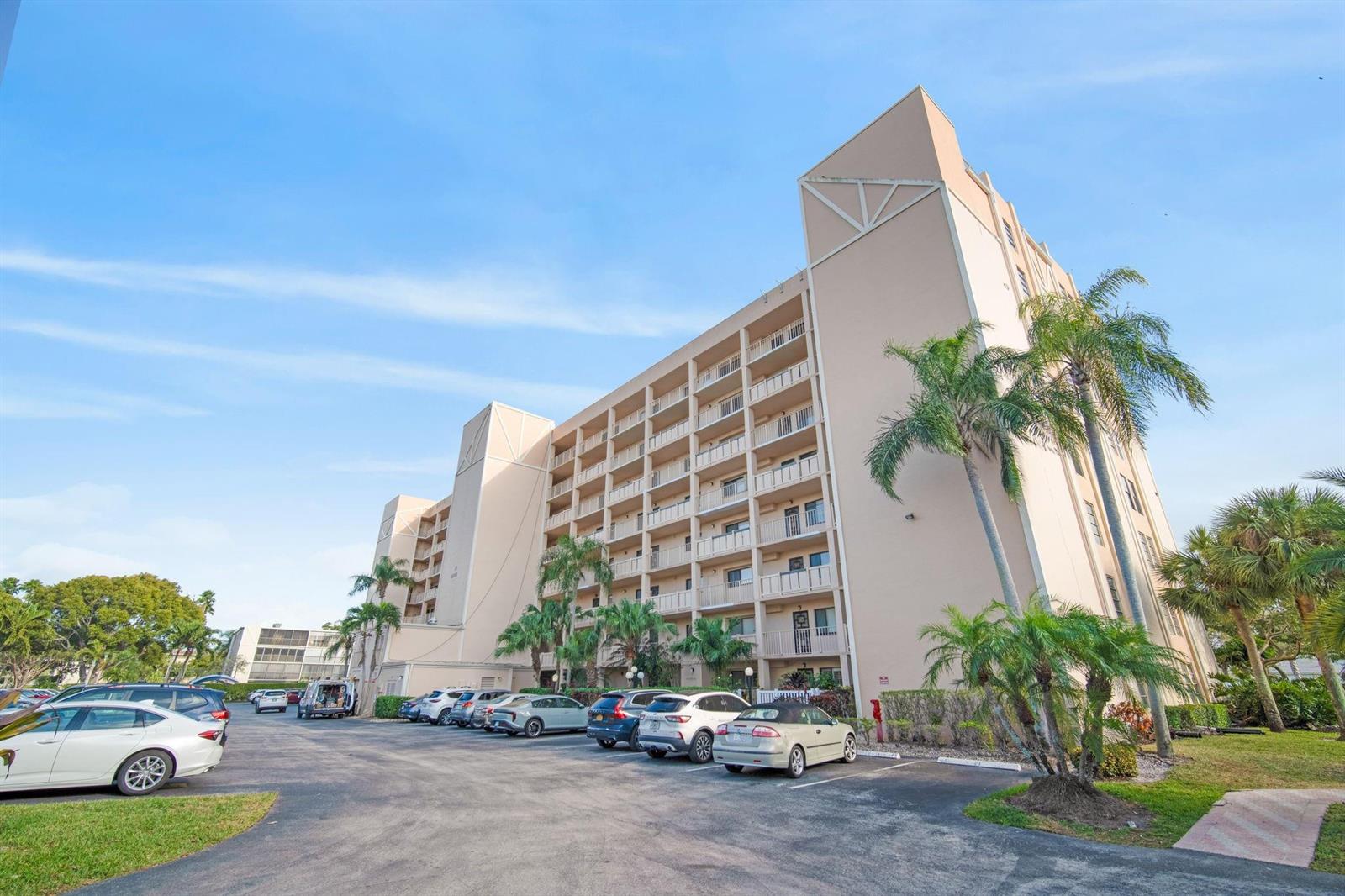 A multi-story apartment building with balconies stands above a parking lot filled with cars — 6866 Huntington Lane # 304, Delray Beach FL 33446, DELRAY BEACH, FL