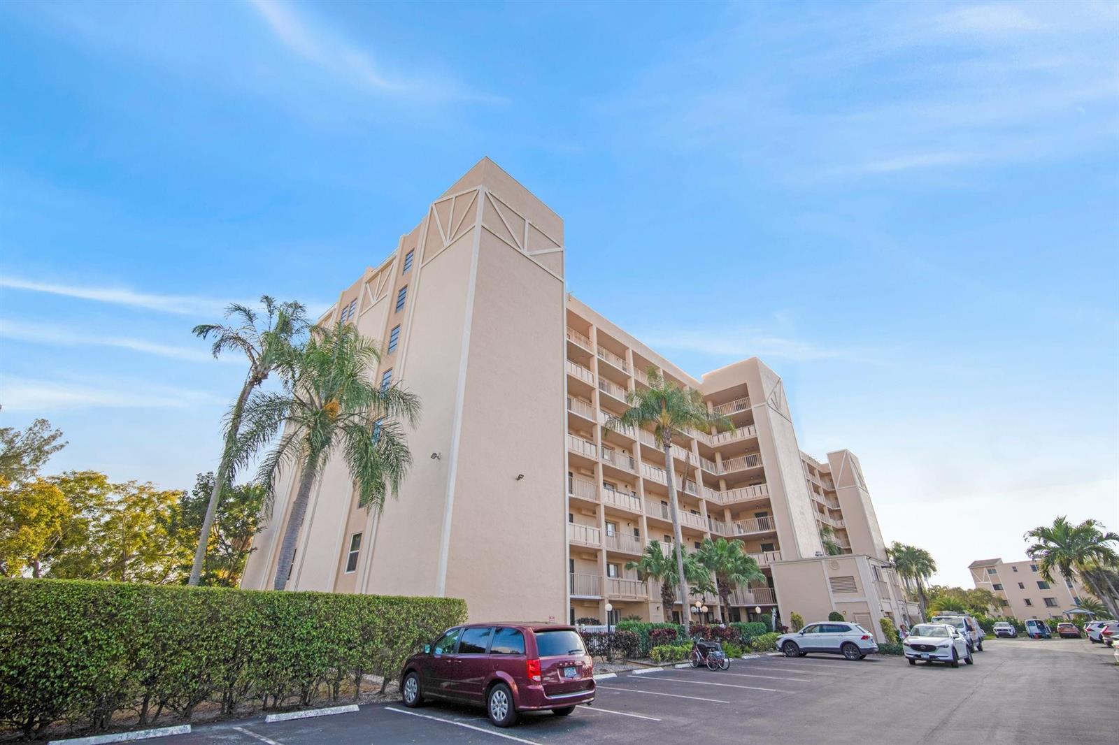 A multi-story beige apartment building with balconies stands above a parking lot with several cars — 6866 Huntington Lane # 304, Delray Beach FL 33446, DELRAY BEACH, FL