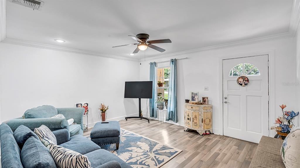 A living room features a blue sofa, a television on a stand, and wood-look flooring — 2906 FIELDCREST COURT, ORLANDO, FL