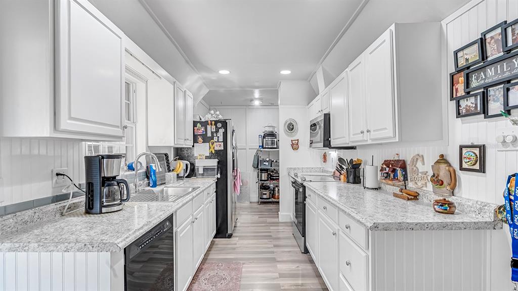 A galley kitchen features white cabinets, speckled countertops, stainless steel appliances, and light wood flooring — 2906 FIELDCREST COURT, ORLANDO, FL