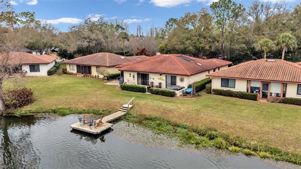 An aerial view shows several single-story homes with tile roofs situated along a small lake — 1007 ROLLING WOODS LANE, LAKELAND, FL