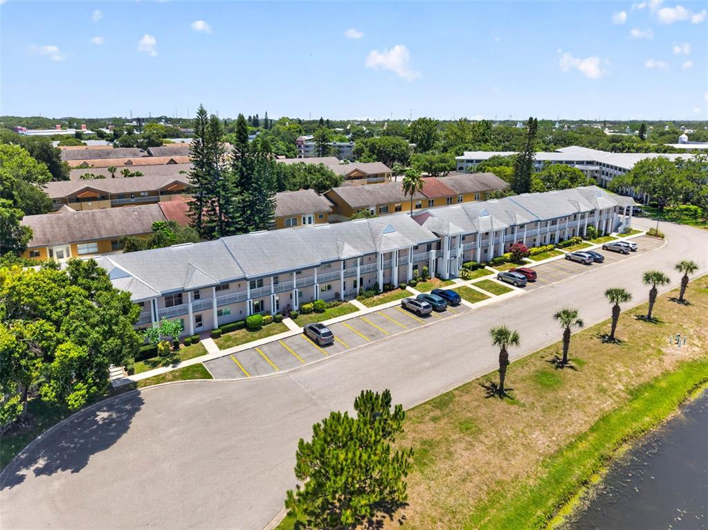 An aerial view shows a multi-story apartment building with a parking lot and pond — 2291 AMERICUS BOULEVARD W UNIT 25, CLEARWATER, FL