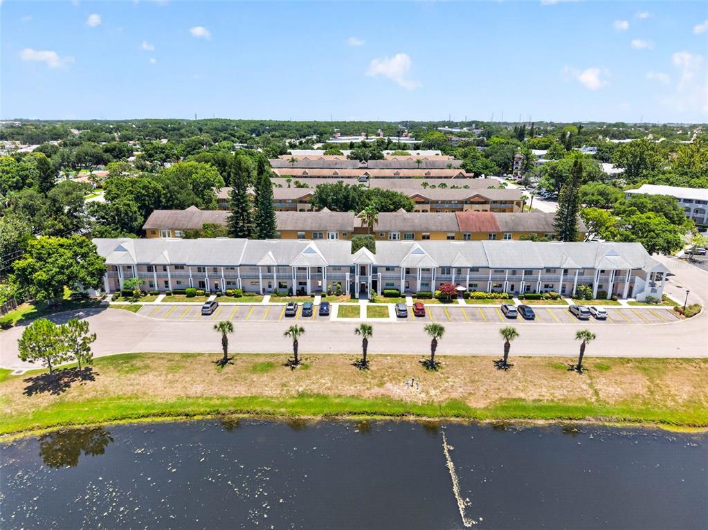 An aerial view of a multi-story apartment complex situated beside a pond — 2291 AMERICUS BOULEVARD W UNIT 25, CLEARWATER, FL