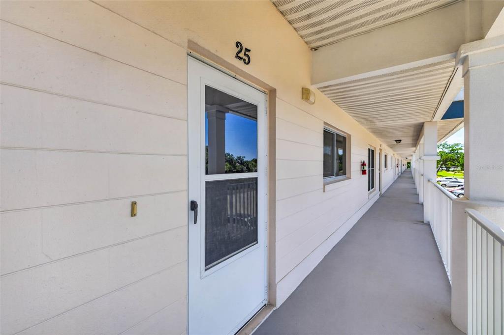 An exterior walkway leads past a white door labeled 25 at a multi-unit building — 2291 AMERICUS BOULEVARD W UNIT 25, CLEARWATER, FL