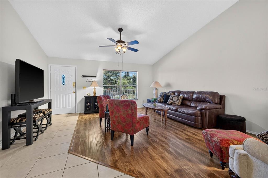 A living room features wood-look flooring, a brown leather sofa, and two patterned armchairs — 2291 AMERICUS BOULEVARD W UNIT 25, CLEARWATER, FL