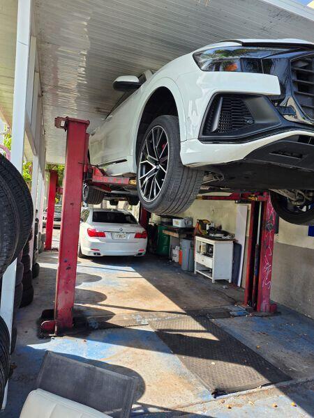A white car is elevated on a hydraulic lift inside an automotive repair shop — 3198 S Dixie Highway, Miami FL 33133, MIAMI, FL