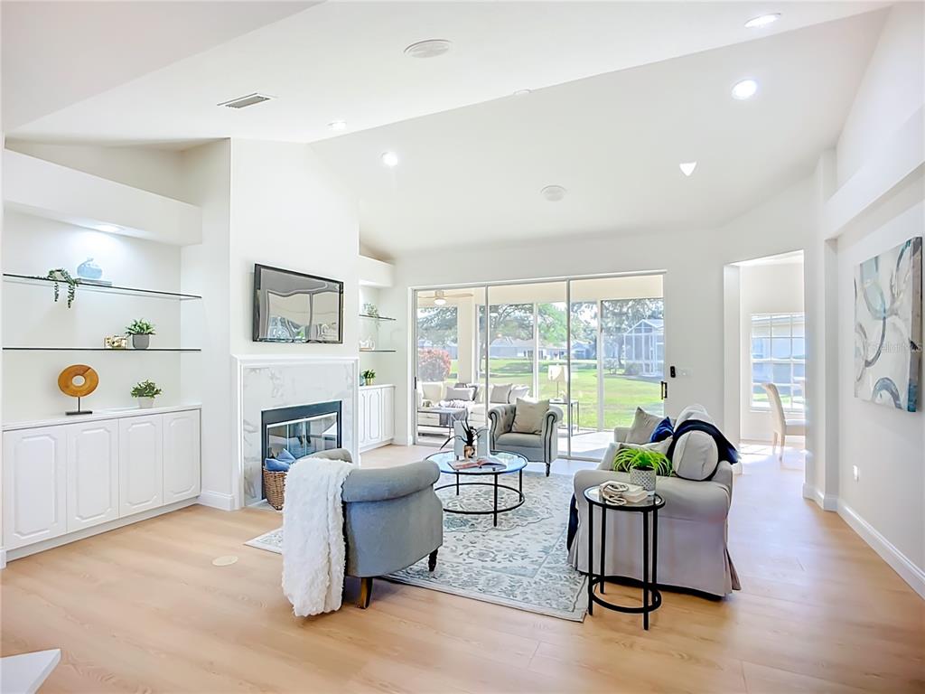 A bright living room features a fireplace, built-in shelving, and sliding glass doors to a patio — 2960 SANDRINGHAM PLACE, SARASOTA, FL