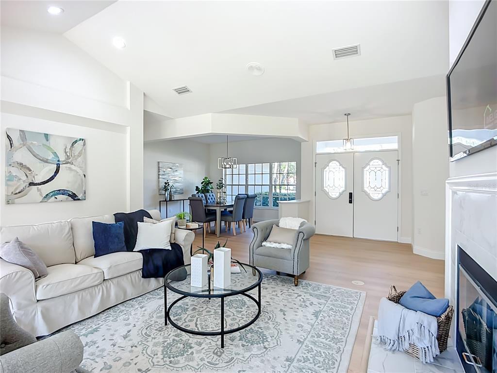 A living room with a fireplace, sofa, and dining area features light wood-look flooring — 2960 SANDRINGHAM PLACE, SARASOTA, FL