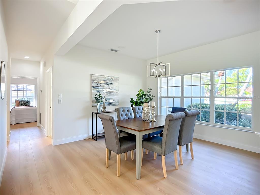 A dining room features a wooden table, gray upholstered chairs, and large windows — 2960 SANDRINGHAM PLACE, SARASOTA, FL