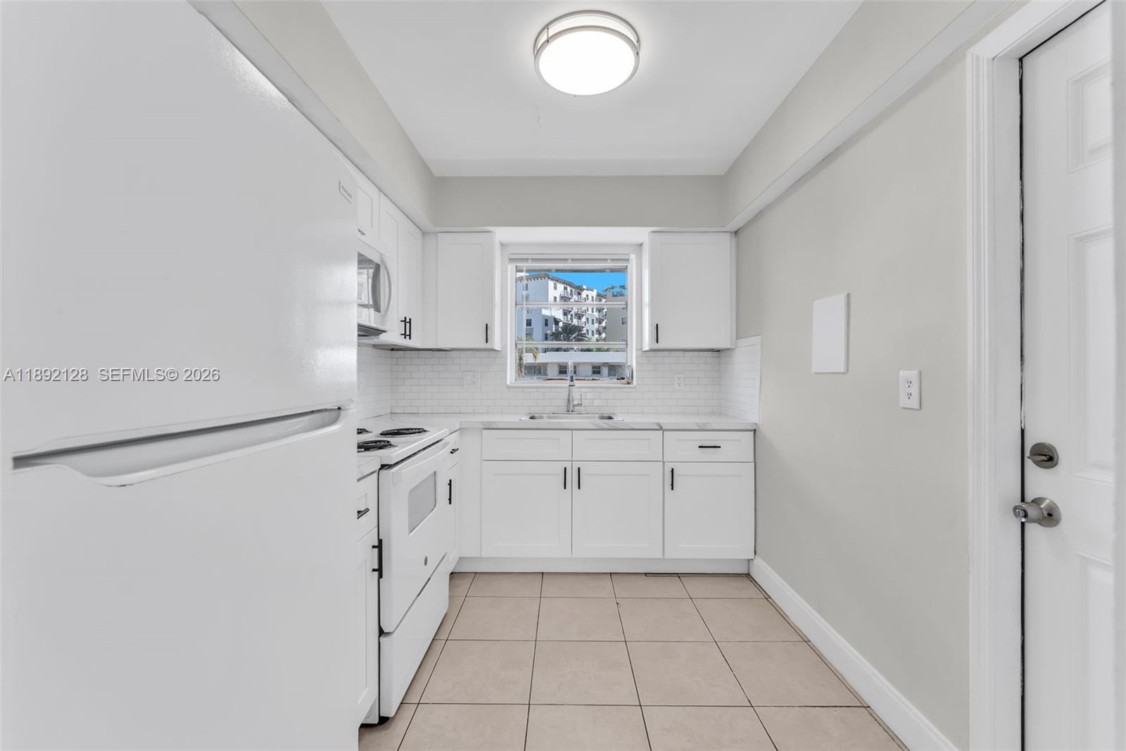 A white kitchen features tile flooring, white cabinets, a subway tile backsplash, and a window — 7330 SW 82nd St # B218, Miami FL 33143, MIAMI, FL
