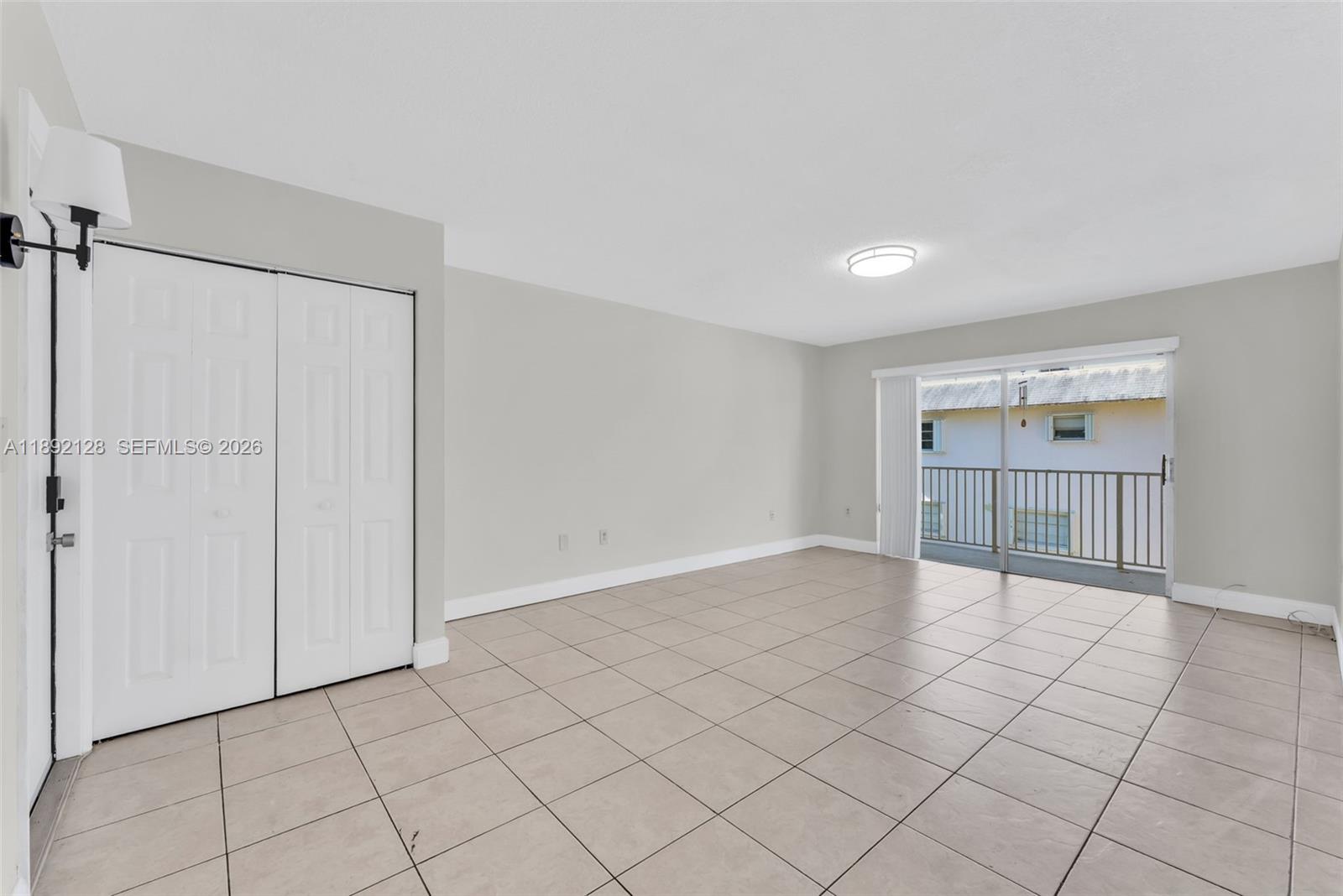 An empty room features light-colored tile flooring, white walls, a closet, and a sliding glass door — 7330 SW 82nd St # B218, Miami FL 33143, MIAMI, FL