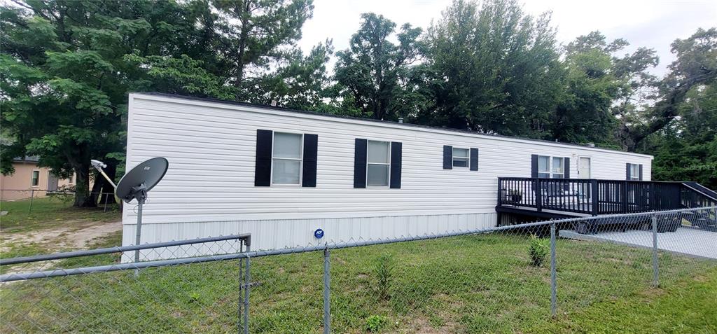 A white mobile home with a black deck and a satellite dish sits behind a fence — 4030 NE 212TH TERRACE, WILLISTON, FL