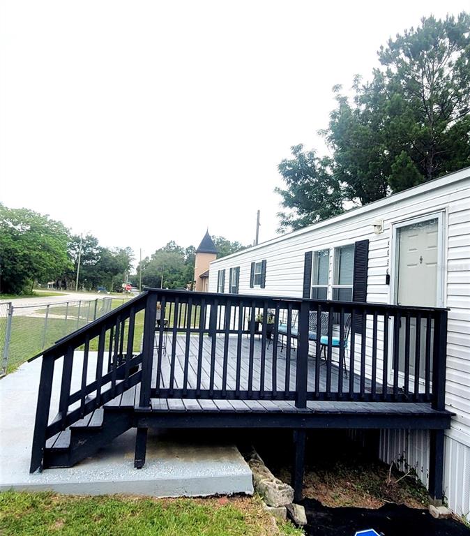 A white mobile home features a black wooden deck with stairs leading to a concrete pad — 4030 NE 212TH TERRACE, WILLISTON, FL