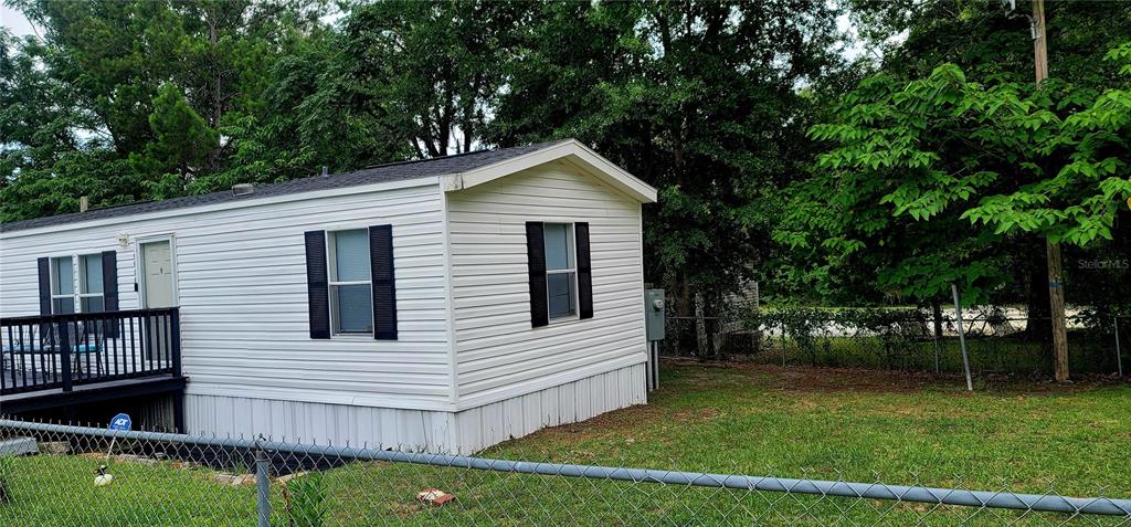 A white mobile home with a wooden deck sits on a grassy lot with trees — 4030 NE 212TH TERRACE, WILLISTON, FL