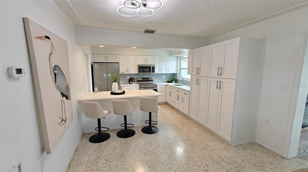 A modern kitchen features white cabinets, a breakfast bar with three stools, and terrazzo flooring — 8521 42ND AVENUE N, ST PETERSBURG, FL