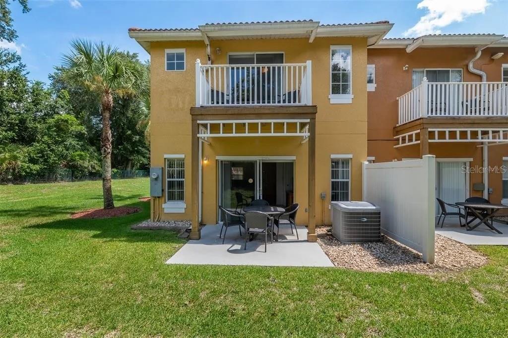 The exterior rear view of a two-story yellow townhouse features a patio and upper balcony — 1055 PARK RIDGE CIRCLE, KISSIMMEE, FL