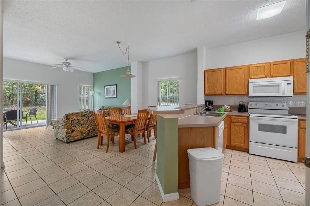 An open-concept kitchen and dining area with tile flooring, wood cabinets, and a sliding glass door — 1055 PARK RIDGE CIRCLE, KISSIMMEE, FL