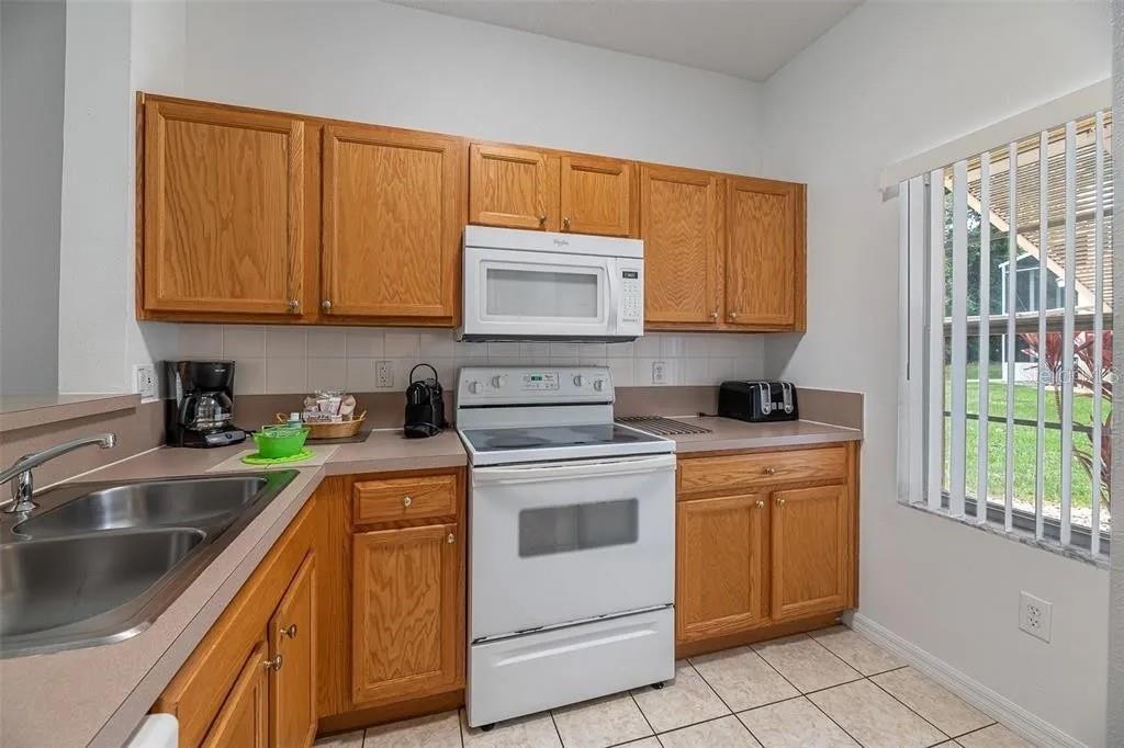 A kitchen features oak cabinets, white appliances, a double sink, and tile flooring — 1055 PARK RIDGE CIRCLE, KISSIMMEE, FL