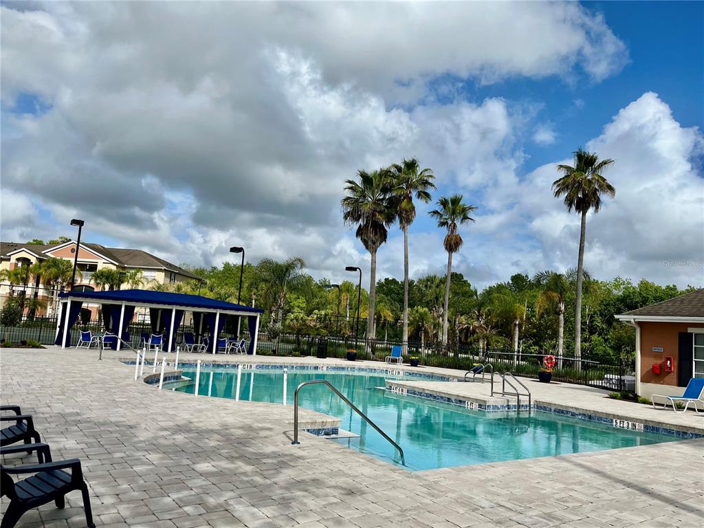 A swimming pool with a blue canopy and palm trees under a cloudy sky — 1939 SUMMER CLUB APT DRIVE UNIT 315, OVIEDO, FL