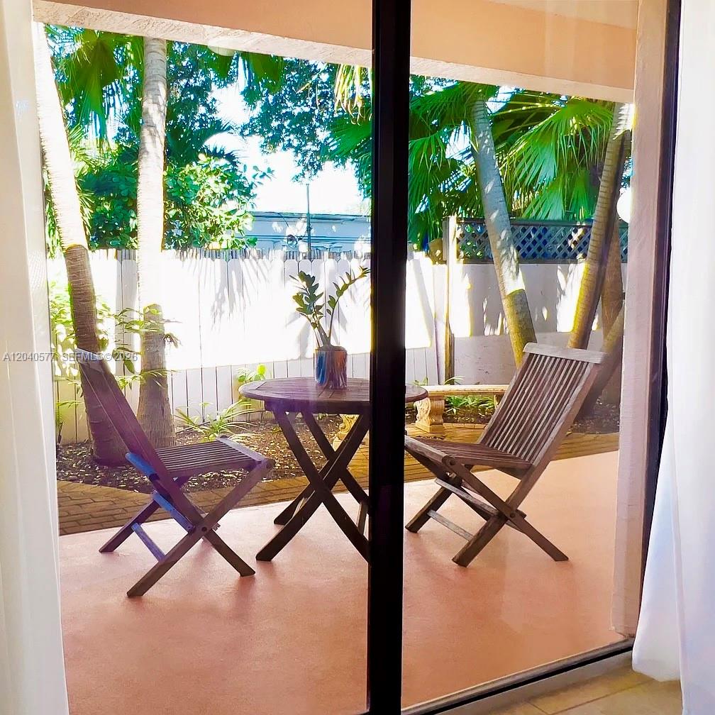 A patio with a wooden table and two chairs viewed through a sliding glass door — 585 NE 66th St # 3, Miami FL 33138, MIAMI, FL