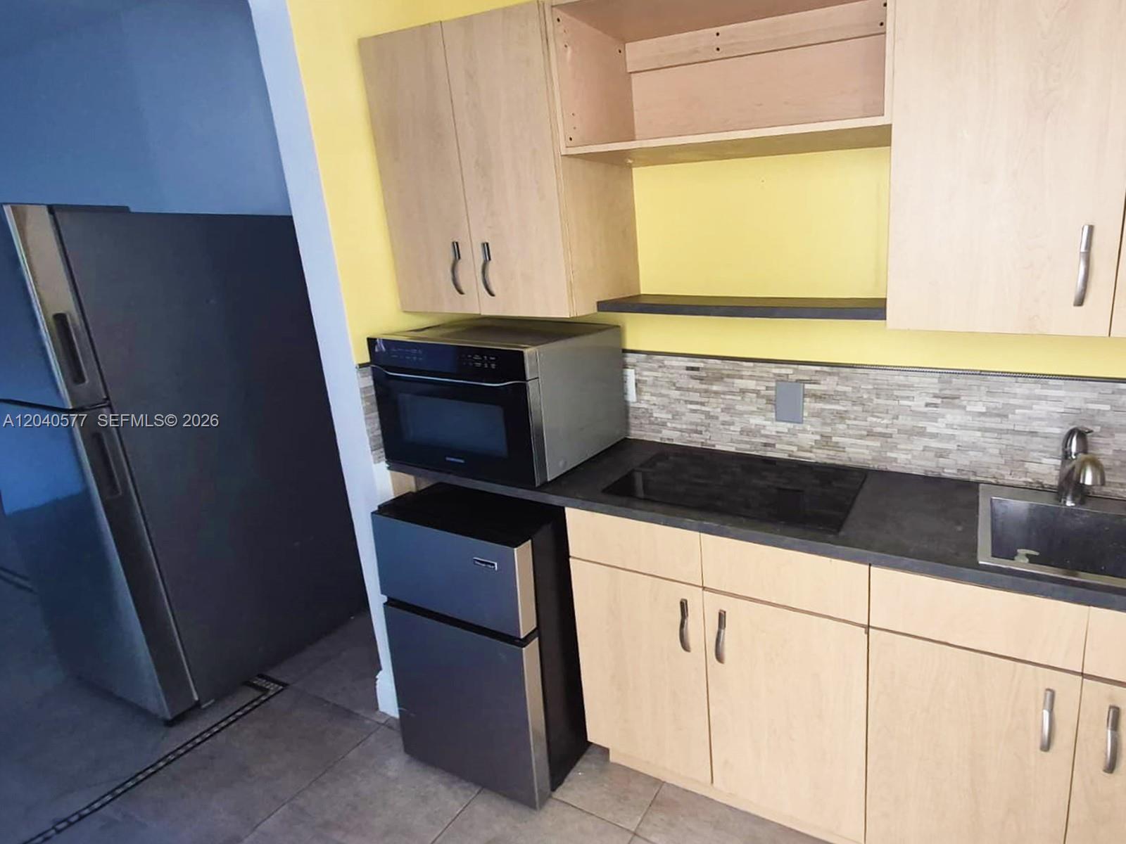 A small kitchen features light wood cabinets, a microwave, a mini-fridge, and a sink — 585 NE 66th St # 3, Miami FL 33138, MIAMI, FL