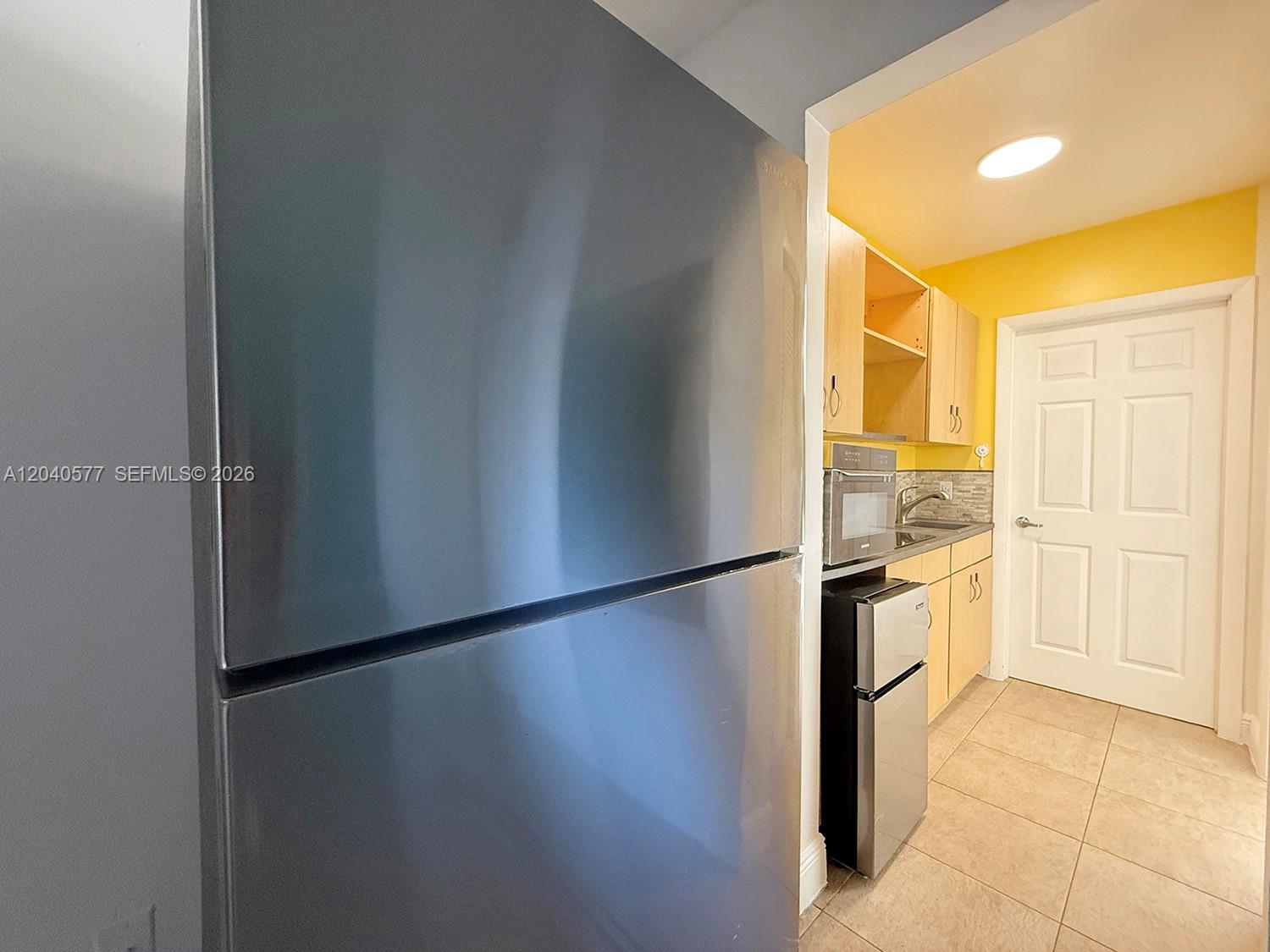 A kitchen features a large refrigerator, a mini-fridge, light wood cabinets, and yellow walls — 585 NE 66th St # 3, Miami FL 33138, MIAMI, FL