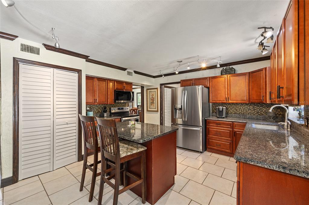 A kitchen features wood cabinets, granite countertops, a center island with seating, and stainless appliances — 16353 NW 130 STREET, WILLISTON, FL