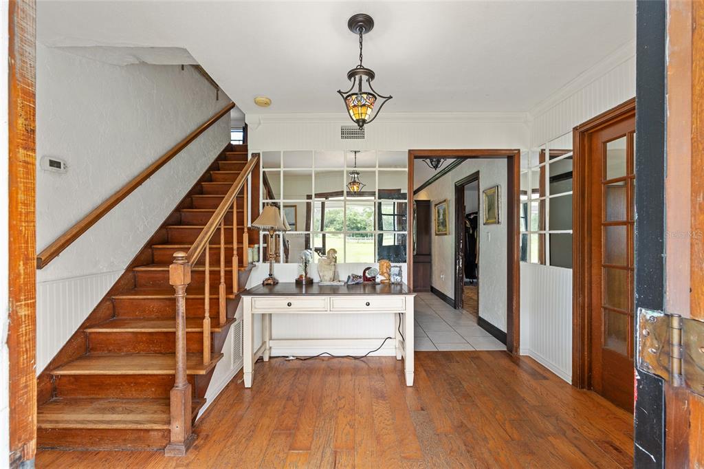 An entryway features a wooden staircase, a console table, and a mirrored wall partition — 16353 NW 130 STREET, WILLISTON, FL