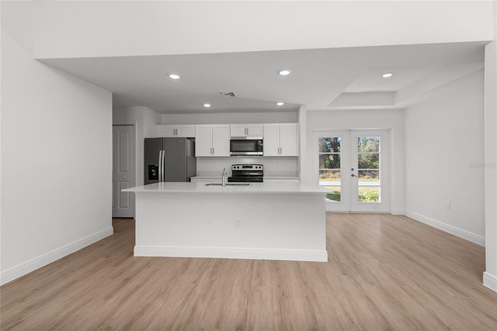 A modern kitchen features white cabinetry, a central island, and light wood-look flooring — 4668 ADDLEY AVENUE, NORTH PORT, FL