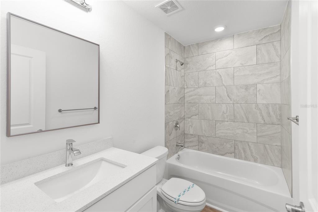 A bathroom features a white vanity, a mirror, a toilet, and a tiled shower-tub combination — 4668 ADDLEY AVENUE, NORTH PORT, FL