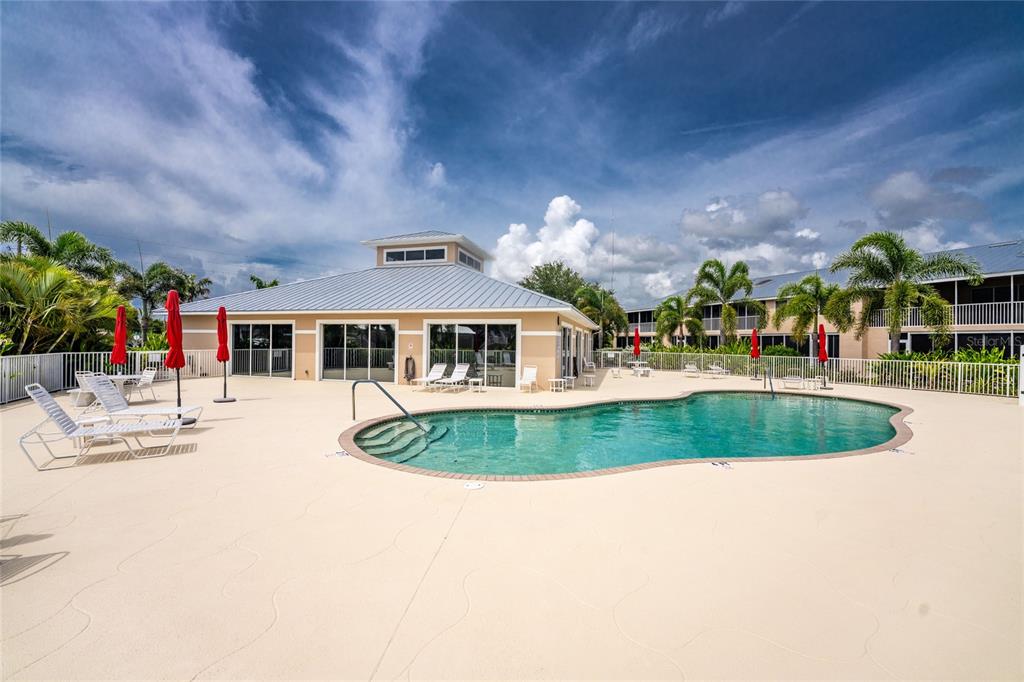 A swimming pool sits on a large patio in front of a community clubhouse building — 9500 FIDDLERS GREEN CIRCLE UNIT 101, ROTONDA WEST, FL