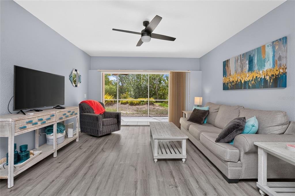 A living room features gray wood-look flooring, a beige sofa, and a sliding glass door — 9500 FIDDLERS GREEN CIRCLE UNIT 101, ROTONDA WEST, FL