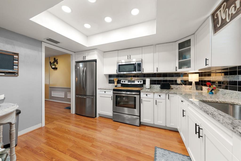 A kitchen features white cabinets, stainless steel appliances, granite countertops, and a black tile backsplash — 1651 S LAKE AVENUE UNIT 3, CLEARWATER, FL
