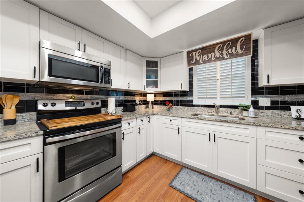 A kitchen features white cabinets, stainless steel appliances, granite countertops, and a black tile backsplash — 1651 S LAKE AVENUE UNIT 3, CLEARWATER, FL