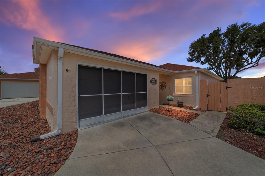 A single-story house exterior features a screened garage, a concrete driveway, and a wooden gate — 911 MEDIRA DRIVE, LADY LAKE, FL