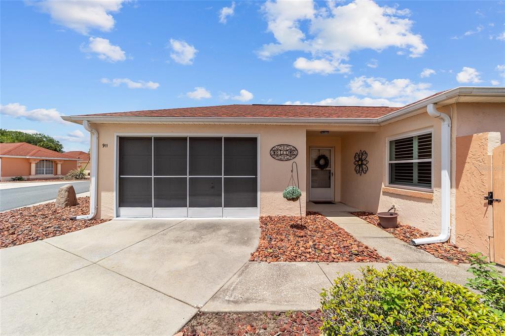 The exterior of a single-story house features a screened garage, a front entrance, and landscaping — 911 MEDIRA DRIVE, LADY LAKE, FL