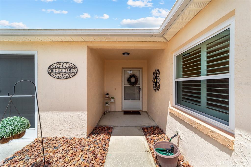 A concrete walkway leads to the covered front entryway of a light-colored stucco home — 911 MEDIRA DRIVE, LADY LAKE, FL