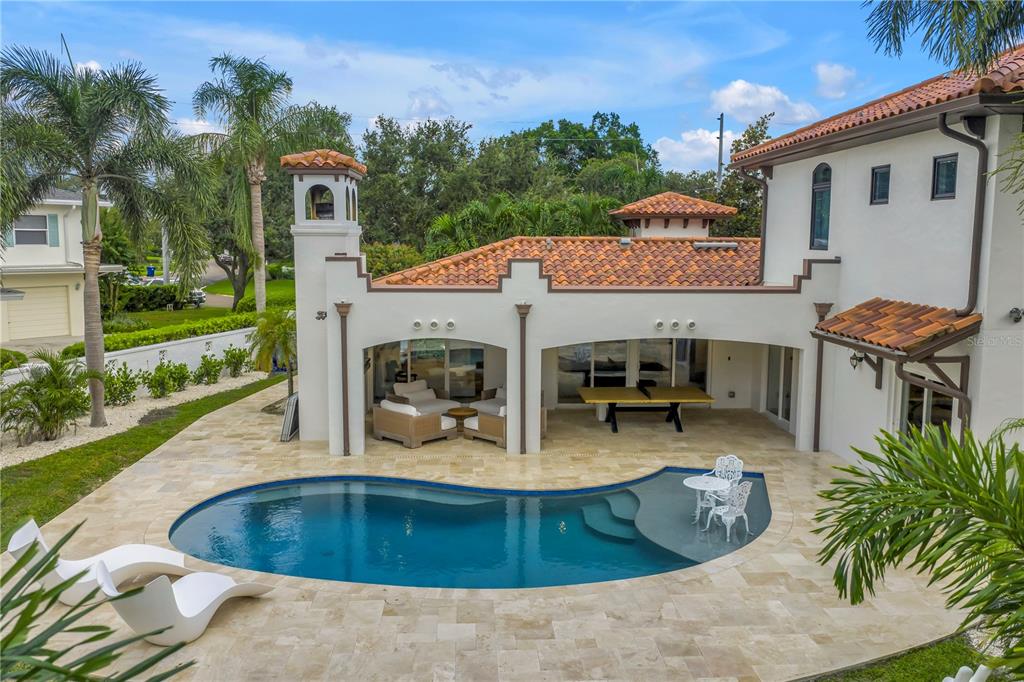 A backyard features a curved swimming pool, a covered patio with furniture, and a house — 145 BAY POINT DRIVE NE, ST PETERSBURG, FL