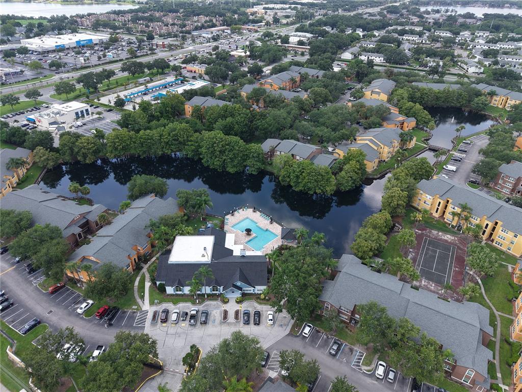 An aerial view shows an apartment complex with a central pool, lake, and parking lots — 4572 COMMANDER DRIVE UNIT 1213, ORLANDO, FL