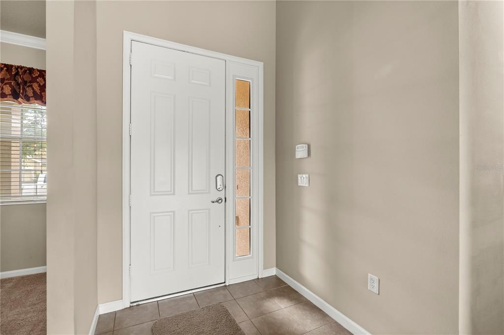 An entryway features a white front door with a sidelight, beige walls, and tiled flooring — 2355 SABASTIAN STREET, MOUNT DORA, FL