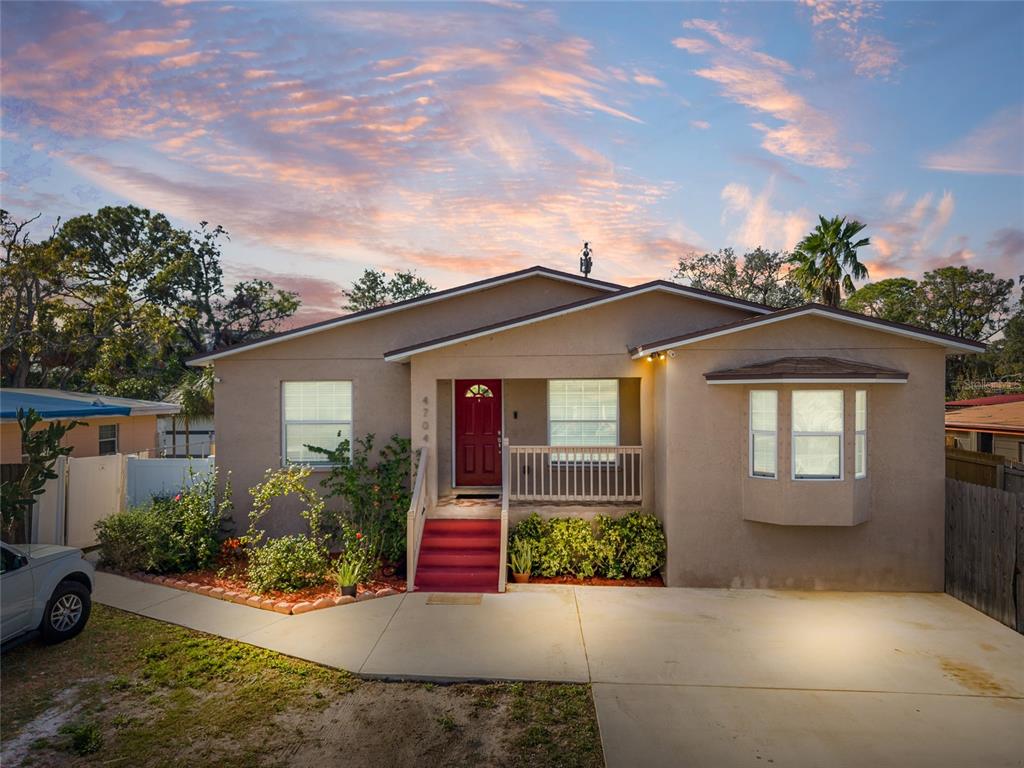 A single-story tan house with a red front door and a concrete driveway at sunset — 4704 TOWN N COUNTRY BOULEVARD, TAMPA, FL